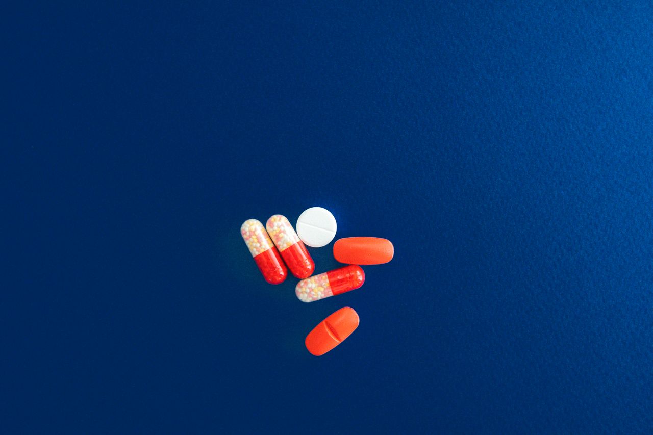 Assorted red and white capsules and tablets on a vivid blue surface.